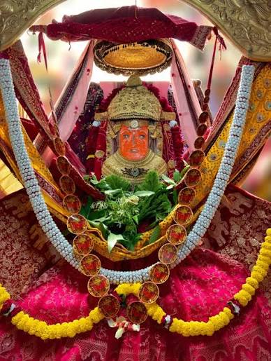 Jeen Mata adorned with golden crown, pearl and gold-medallion garland, marigold strands and fresh green leaves, blessing her devotees