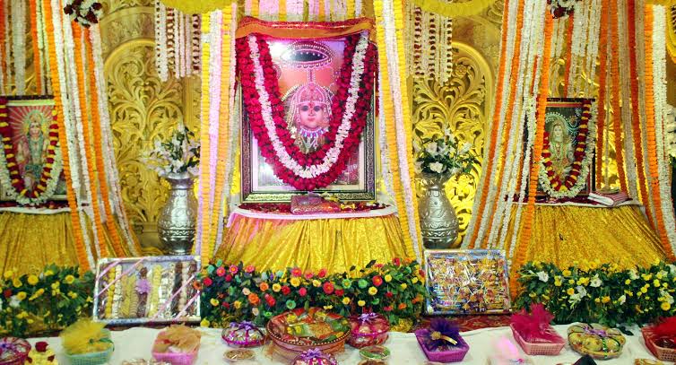 Navratri bhog darbar of Jeen Mata in a golden hall with marigold and white flower strands, silver vases and tables of sweets, dry fruits and fruit baskets
